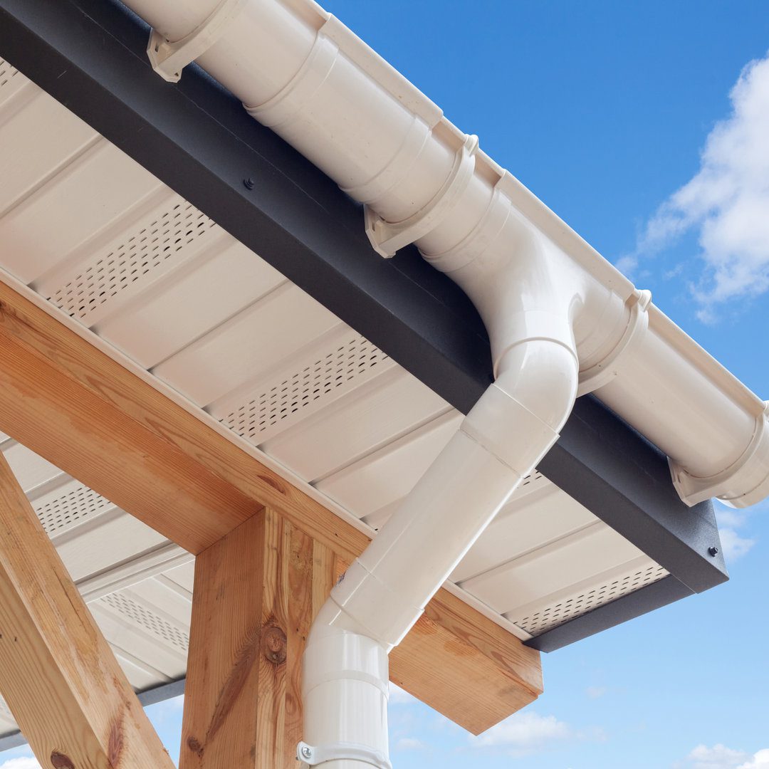 New white rain gutter SIP panel house construction. New white rain gutter. Drainage System with Plastic Siding Soffits and Eaves against blue sky